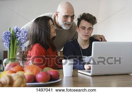 Family discussing while looking at laptop on table at home View Large Photo Image Stock Image - Family discussing while looking at laptop on table at home. Fotosearch