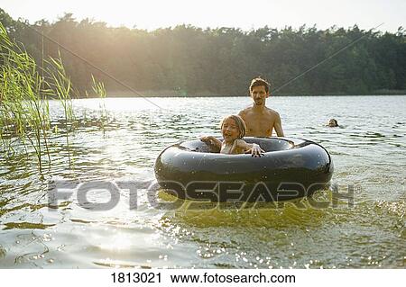 Stock Image - Father and daughter playing with inner tube in sunny summer lake. Fotosearch