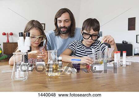 Stock Photo - Father assisting children in doing school science project at home. Fotosearch