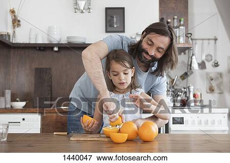 Stock Photo - Father assisting daughter squeeze oranges in kitchen. Fotosearch