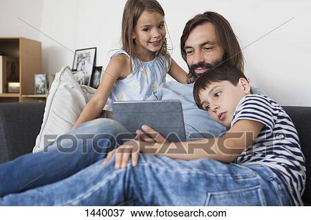 Father with children using digital tablet on sofa at home View Large Photo Image Stock Photo - Father with children using digital tablet on sofa at home. Fotosearch
