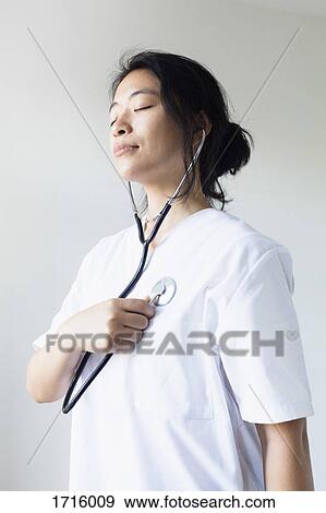 Stock Photo - Female doctor listening self heart beat with stethoscope against wall. Fotosearch