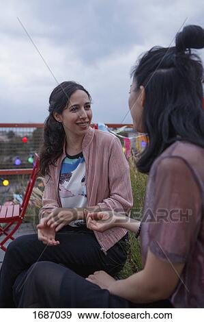 Female friends talking while sitting on patio View Large Photo Image Stock Photo - Female friends talking while sitting on patio. Fotosearch