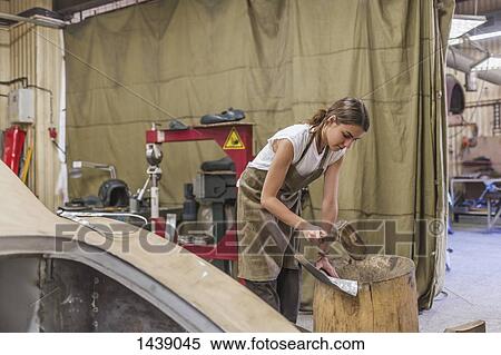 Stock Photography - Female mechanic hitting metal on wooden barrel at garage. Fotosearch