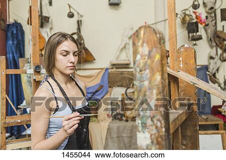 Female painter holding paintbrush and looking at easel at studio View Large Photo Image Picture - Female painter holding paintbrush and looking at easel at studio. Fotosearch