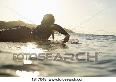 Female surfer paddling out on sunny, sunset ocean View Large Photo Image Stock Photo - Female surfer paddling out on sunny, sunset ocean. Fotosearch