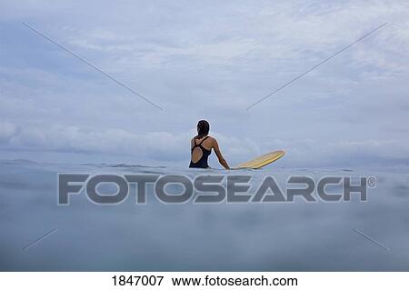 Female surfer straddling surfboard in ocean View Large Photo Image Stock Photo - Female surfer straddling surfboard in ocean. Fotosearch