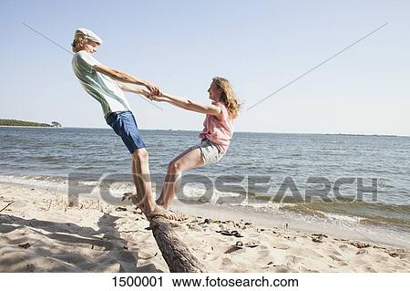 Friends holding hands while standing on driftwood at beach against clear sky View Large Photo Image Stock Image - Friends holding hands while standing on driftwood at beach against clear sky. Fotosearch