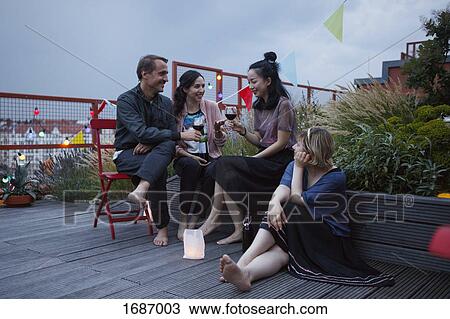 Friends talking while holding wineglasses on patio at dusk View Large Photo Image Stock Image - Friends talking while holding wineglasses on patio at dusk. Fotosearch