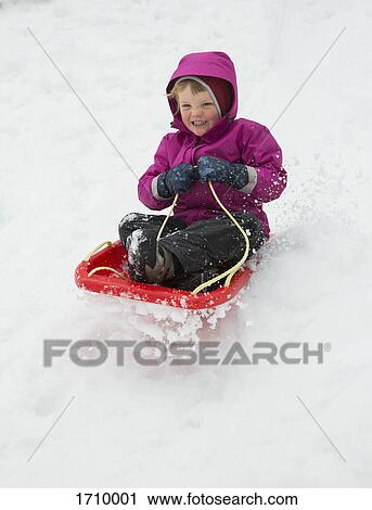 Stock Image - Full length of boy tobogganing on snow covered field. Fotosearch