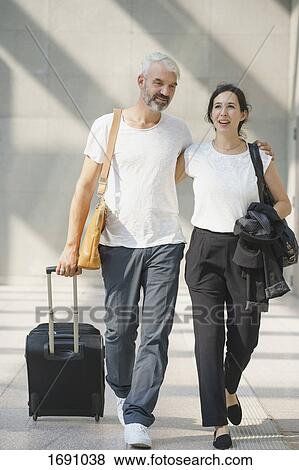 Full length of business couple with wheeled luggage walking at airport View Large Photo Image Stock Photo - Full length of business couple with wheeled luggage walking at airport. Fotosearch