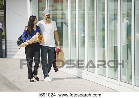 Full length of couple walking on sidewalk by glass wall in city on sunny day View Large Photo Image Picture - Full length of couple walking on sidewalk by glass wall in city on sunny day. Fotosearch