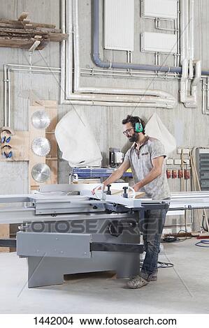 Full length of male carpenter using a sliding table saw in workshop View Large Photo Image Picture - Full length of male carpenter using a sliding table saw in workshop. Fotosearch