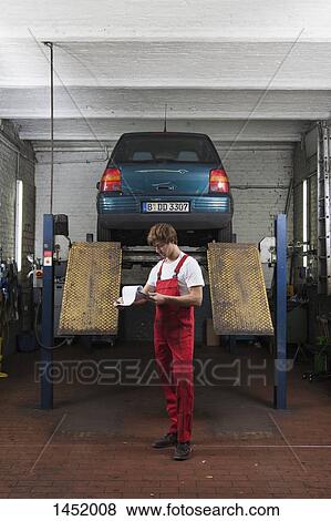 Full length of mechanic reviewing documents while standing at garage View Large Photo Image Stock Photo - Full length of mechanic reviewing documents while standing at garage. Fotosearch