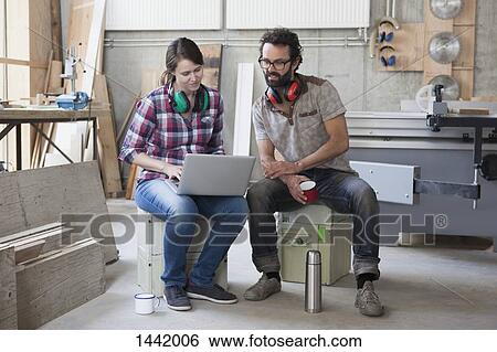 Stock Photograph - Full length of mid adult carpenters using laptop in workshop. Fotosearch