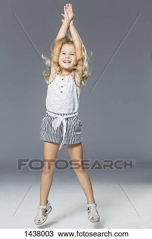 Stock Image - Full length of playful girl jumping against gray wall. Fotosearch