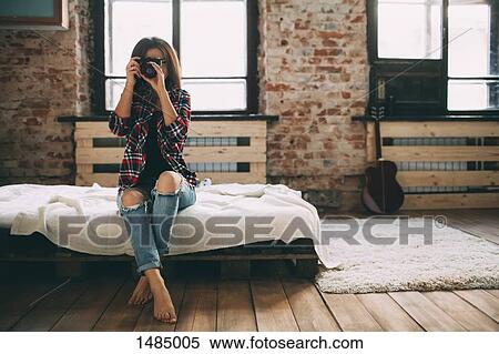Stock Photography - Full length of woman photographing through SLR camera in bedroom at home. Fotosearch