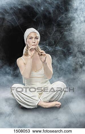 Stock Image - Full length of woman playing flute while surrounded with smoke. Fotosearch