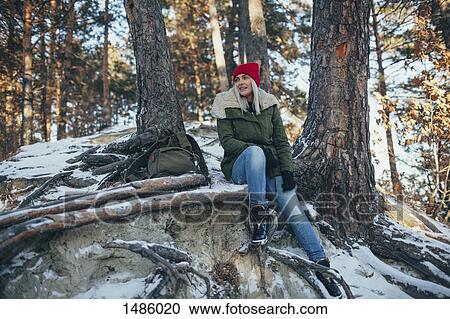 Stock Image - Full length of young woman sitting in snow covered forest. Fotosearch