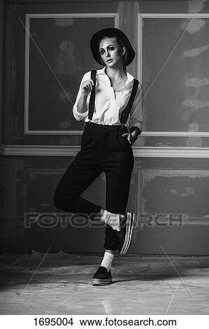 Full length of young woman wearing suspenders standing against wall View Large Photo Image Picture - Full length of young woman wearing suspenders standing against wall. Fotosearch