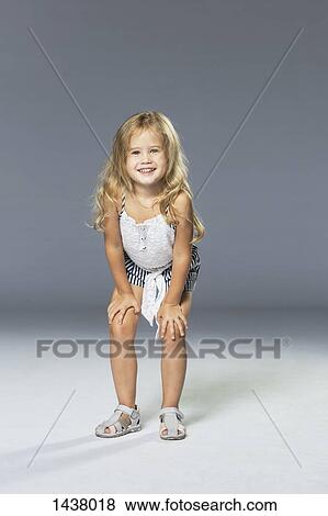 Full length portrait of happy girl standing with hands on knees against gray wall View Large Photo Image Stock Photo - Full length portrait of happy girl standing with hands on knees against gray wall. Fotosearch