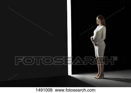 Stock Photo - Full length pregnant woman looking through opening in wall. Fotosearch