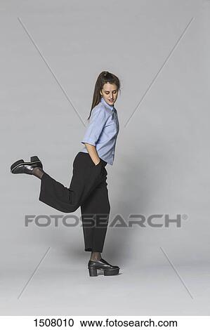 Full length woman standing on one leg with hands in pockets against gray background View Large Photo Image Stock Image - Full length woman standing on one leg with hands in pockets against gray background. Fotosearch