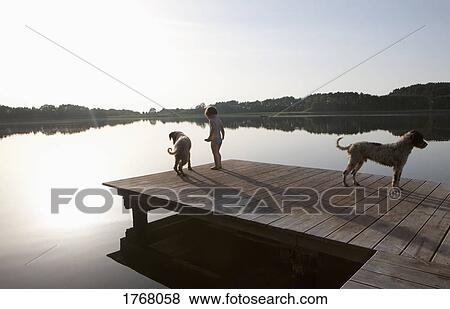 Stock Photo - Girl and dogs on lakeside dock. Fotosearch