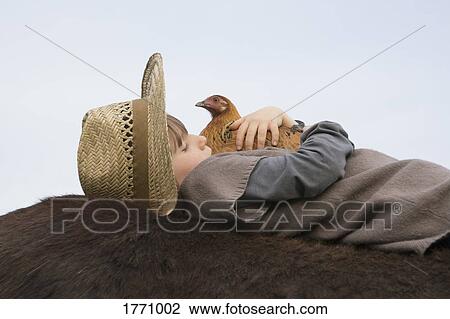 Stock Image - Girl hugging chicken, laying on horse. Fotosearch