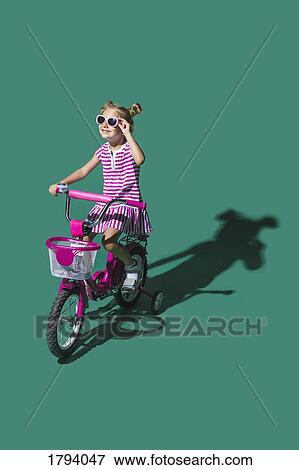 Stock Photo - Girl in sunglasses bike riding against green background. Fotosearch