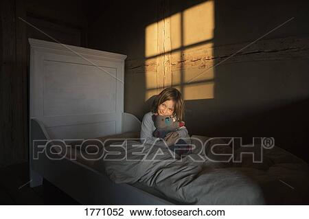 Stock Image - Girl laying in bed with teddy bear. Fotosearch