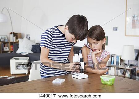 Girl looking at brother using microscope at table in house View Large Photo Image Stock Photo - Girl looking at brother using microscope at table in house. Fotosearch