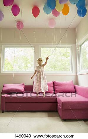 Girl reaching for balloons while standing on sofa at home View Large Photo Image Stock Image - Girl reaching for balloons while standing on sofa at home. Fotosearch