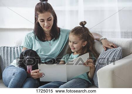 Girl reading book by mother and dog on sofa at home View Large Photo Image Stock Photography - Girl reading book by mother and dog on sofa at home. Fotosearch