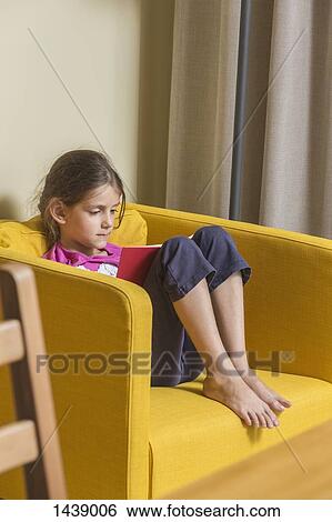 Girl reading book while sitting on armchair at home View Large Photo Image Stock Photograph - Girl reading book while sitting on armchair at home. Fotosearch