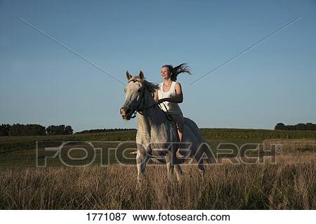 Stock Photo - Girl riding horse in sunny, rural field. Fotosearch