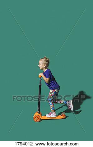 Girl riding scooter on green background View Large Photo Image Stock Image - Girl riding scooter on green background. Fotosearch