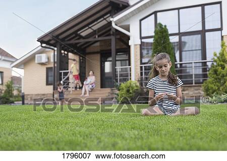 Stock Photo - Girl sitting in grass in backyard. Fotosearch