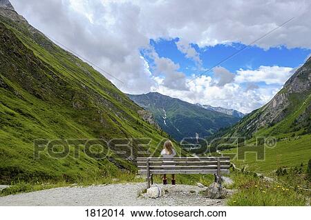 Picture - Girl sitting on bench looking at scenic mountain view, Innergschloess, Tyrol, Austria. Fotosearch
