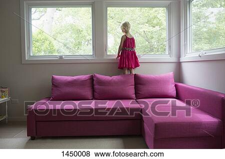 Stock Photo - Girl standing on pink sofa by window at home. Fotosearch