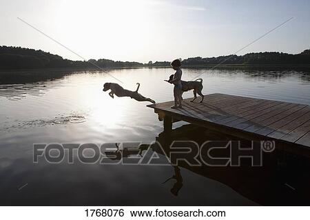 Stock Photograph - Girl watching dog jumping off lakeside dock, Wiendorf, Mecklenburg-Vorpommern, Germany. Fotosearch