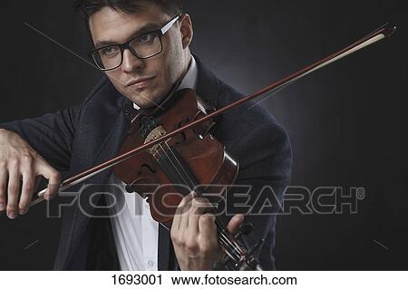 Stock Image - Handsome man wearing formals playing violin against black background. Fotosearch