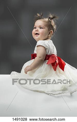 Happy baby girl wearing dress and sitting against gray background View Large Photo Image Stock Photo - Happy baby girl wearing dress and sitting against gray background. Fotosearch