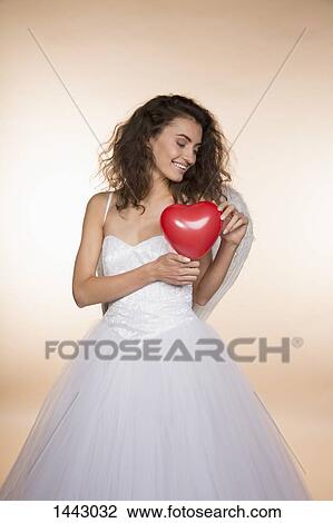 Happy bride holding heart shape balloon against colored background View Large Photo Image Stock Image - Happy bride holding heart shape balloon against colored background. Fotosearch
