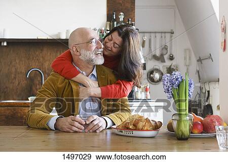 Stock Photo - Happy couple embracing and smiling by table at home. Fotosearch