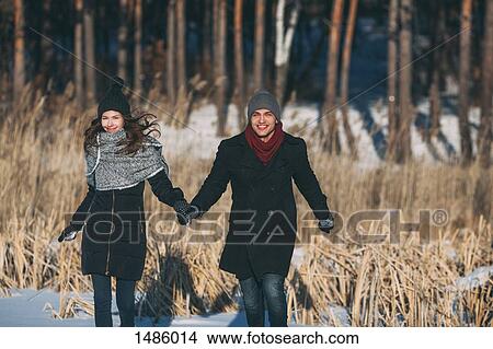 Happy couple holding hands while walking on snow covered field View Large Photo Image Picture - Happy couple holding hands while walking on snow covered field. Fotosearch
