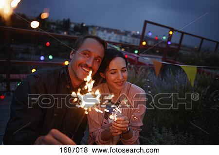 Stock Photo - Happy couple holding sparklers on patio at night. Fotosearch