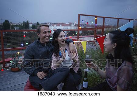 Stock Image - Happy couple talking to female friend holding wine on patio. Fotosearch