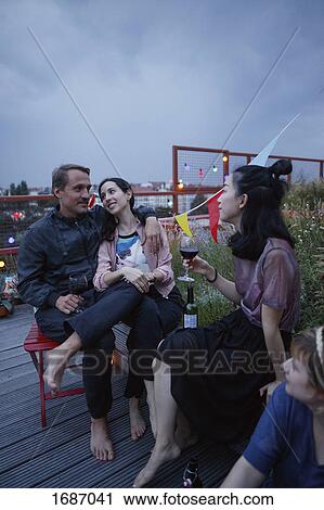 Stock Image - Happy couple talking while sitting with friends on patio at dusk. Fotosearch