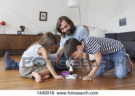 Stock Photo - Happy family looking at boy using microscope on hardwood floor. Fotosearch